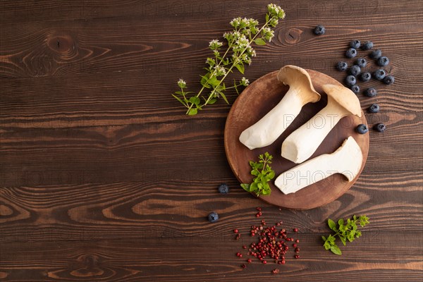 King Oyster mushrooms or Eringi (Pleurotus eryngii) on brown wooden background with blueberry, herbs and spices. Top view, flat lay, copy space