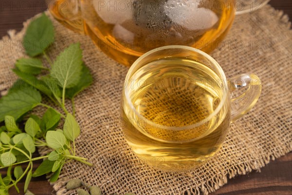 Green oolong tea with herbs in glass on brown wooden background and linen textile. Healthy drink concept. Side view, close up, selective focus