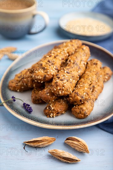 Crumble cookies with seasme and almonds on ceramic plate with cup of coffee and blue linen textile on blue wooden background. side view, close up, selective focus