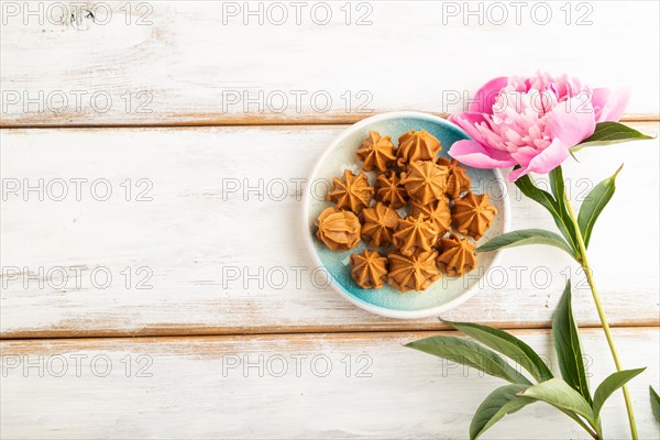 Homemade soft caramel fudge candies on blue plate on white wooden background, peony flower decoration. top view, flat lay, copy space