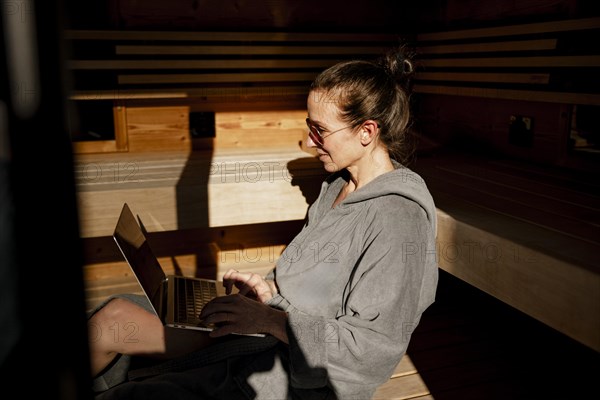 Woman sits with laptop in the sauna