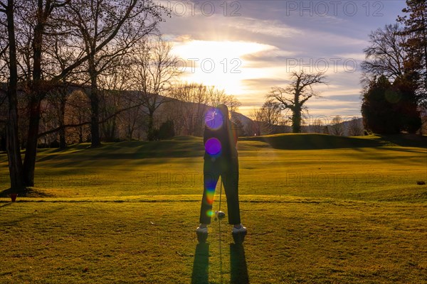 Female Golfer Teeing off with Her Golf Club Driver on Golf Course in Sunset and Lens Flare in Switzerland