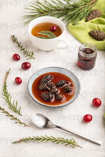 Pine cone jam with herbal tea on gray concrete background and green linen textile. Side view, close up