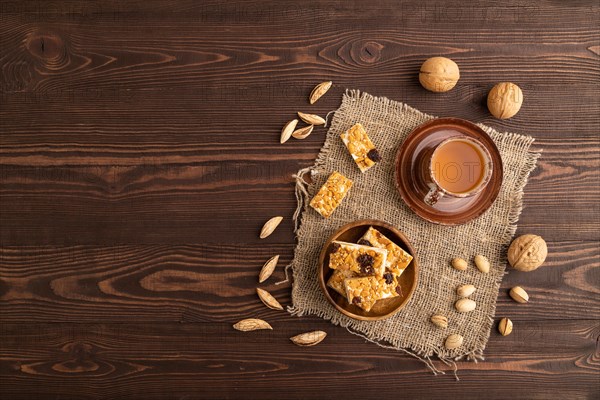 Traditional candy nougat with nuts and sesame with cup of green tea on brown wooden background and linen textile. top view, flat lay, copy space