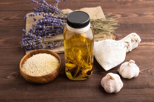 Sunflower oil in a glass jar with various herbs and spices, lavender, sesame, rosemary on a brown wooden background. Side view, close up