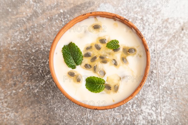 Yoghurt with granadilla and mint in clay bowl on brown concrete background. top view, flat lay, close up