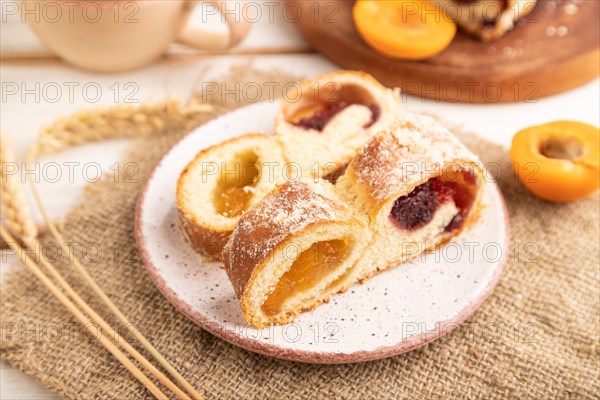 Homemade sweet bun with apricot jam and cup of coffee on white wooden background and linen textile. side view, close up, selective focus