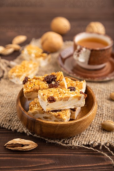 Traditional candy nougat with nuts and sesame with cup of green tea on brown wooden background and linen textile. side view, close up, selective focus