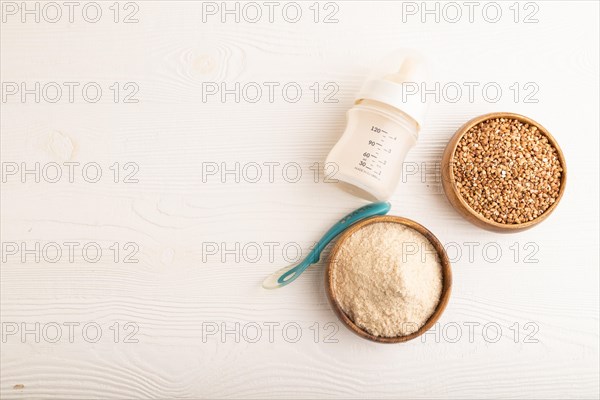 Powdered milk and buckwheat baby food mix, infant formula, pacifier, bottle, spoon on white wooden background. Top view, flat lay, copy space, artificial feeding concept