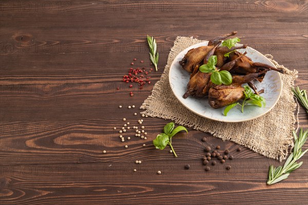 Smoked quails with herbs and spices on a ceramic plate with linen textile on a brown wooden background. Side view, copy space