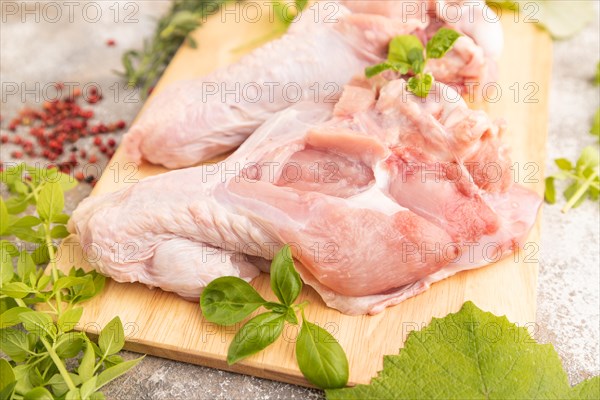 Raw turkey wing with herbs and spices on a wooden cutting board on a brown concrete background. Side view, close up, selective focus