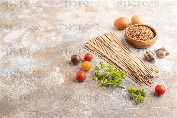Japanese buckwheat soba noodles with tomato, eggs, spices, herbs on brown concrete background. Side view, copy space