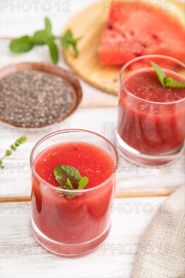 Watermelon juice with chia seeds and mint in glass on a white wooden background with linen textile. Healthy drink concept. Side view, close up, selective focus
