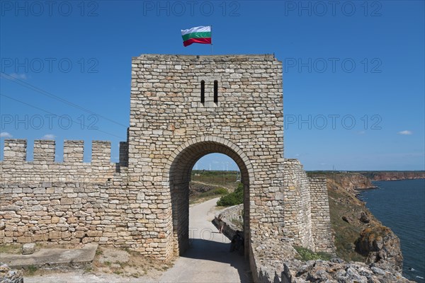 Stone archway of an old fortress with waving flag next to a steep cliff, fortress ruins, Cape Kaliakra, Dobruja, Black Sea, Bulgaria, Europe