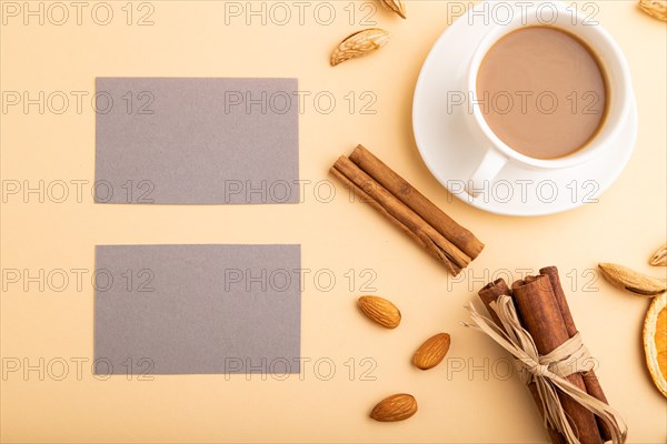 Composition of gray paper business cards, almonds, cinnamon and cup of coffee. mockup on orange background. Blank, top view, still life, flat lay, copy space