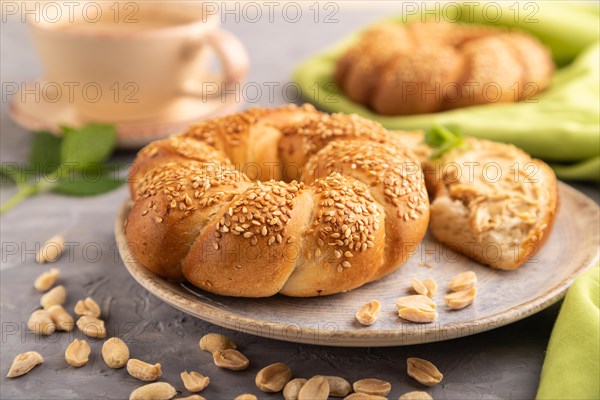 Homemade sweet bun with peanut butter and cup of coffee on a gray concrete background and green linen textile. side view, close up, selective focus