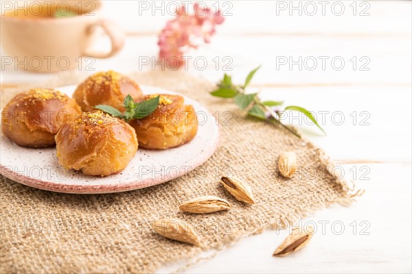 Homemade traditional turkish dessert sekerpare with almonds and honey, cup of green tea on white wooden background and linen textile. side view, close up, selective focus