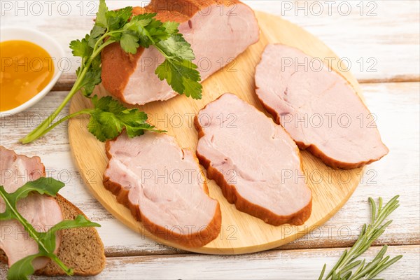 Smoked pork ham on cutting board with pepper and herbs on white wooden background. Side view, close up, selective focus