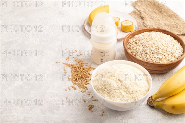 Powdered milk and oatmeal, banana baby food mix, infant formula, pacifier, bottle, spoon on gray concrete background. Side view, copy space, artificial feeding concept