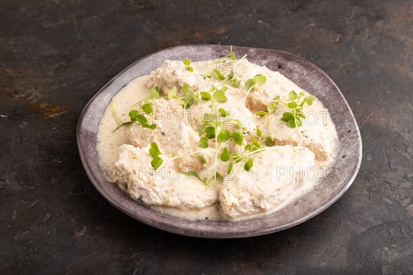 Stewed chicken fillets with coconut milk sauce and rucola microgreen on black concrete background. side view, copy space