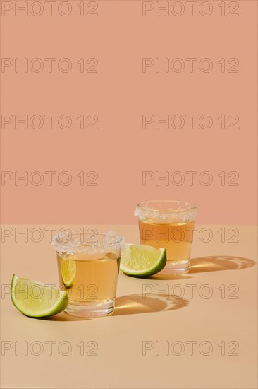Two tequila shots with salt and lime on bright peach color background