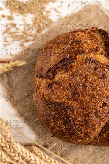Fresh homemade golden grain bread with ears of wheat and rye on white wooden background and linen textile. top view, flat lay, close up