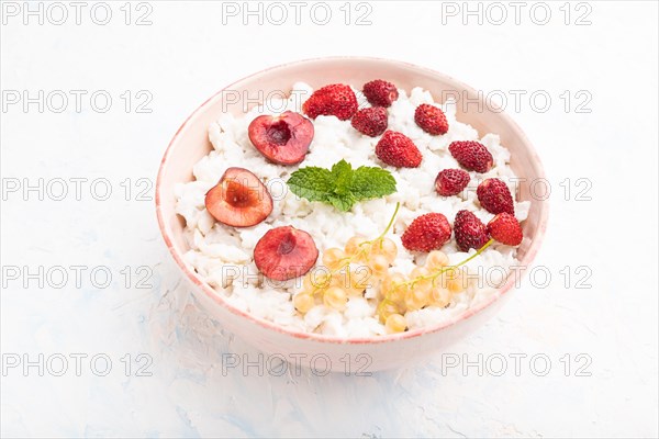 Rice flakes porridge with milk and strawberry in ceramic bowl on white concrete background. Side view, close up