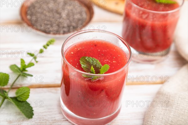 Watermelon juice with chia seeds and mint in glass on a white wooden background with linen textile. Healthy drink concept. Side view, close up, selective focus