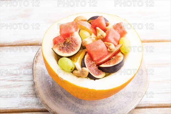 Vegetarian fruit salad of watermelon, grapes, figs, pear, orange, cashew on white wooden background. Side view, close up