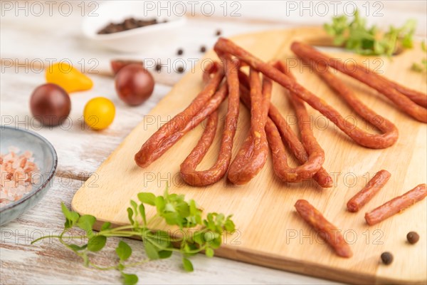 Traditional polish smoked pork sausage kabanos on cutting board with salt and pepper on white wooden background. Side view, close up, selective focus