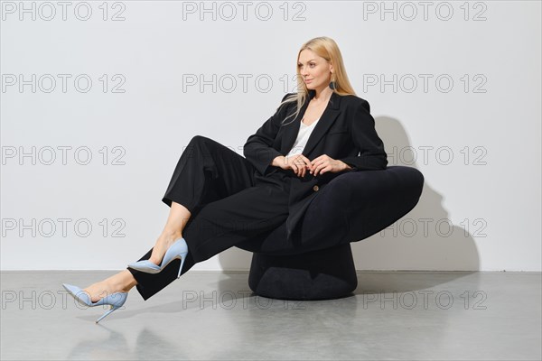 A professional woman in a chic outfit, seated confidently on a black bean bag, exuding elegance and sophistication against white background