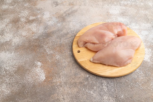 Raw chicken breast on a wooden cutting board on a brown concrete background. Side view, copy space