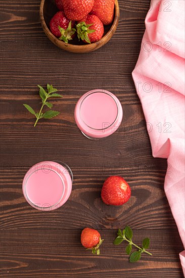 Sweet strawberry liqueur in glass on a brown wooden background and pink textile. top view, close up, flat lay