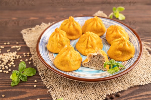 Fried manti dumplings with pepper, basil on brown wooden background and linen textile. Side view, close up