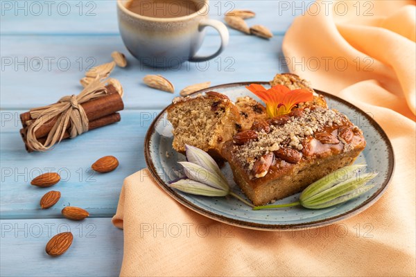 Caramel and almond cake with cup of coffee on blue wooden background and orange linen textile. side view, close up