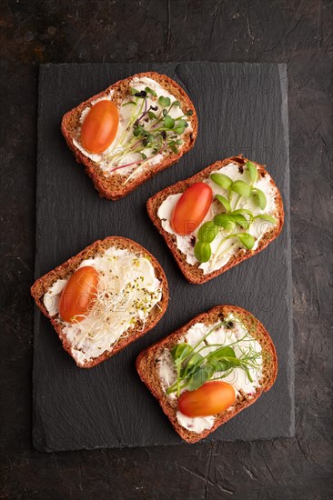 Red beet bread sandwiches with cream cheese, tomatoes and microgreen on black concrete background. top view, flat lay, close up