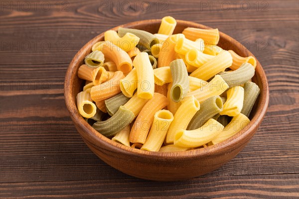 Rigatoni colored raw pasta with tomato, eggs, spices, herbs on brown wooden background. Side view, close up