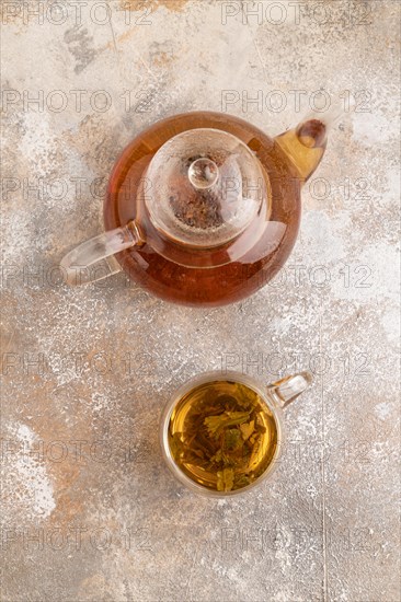 Red tea with herbs in glass teapot on brown concrete background. Healthy drink concept. Top view, flat lay, close up