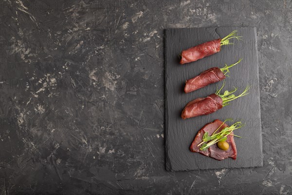 Slices of smoked salted meat with green pea microgreen on black concrete background. Top view, flat lay, copy space