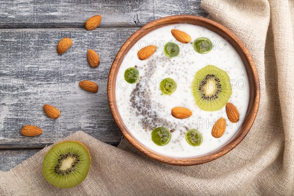 Yogurt with kiwi, gooseberry, chia and almonds in wooden bowl on gray wooden background and linen textile. top view, flat lay, close up