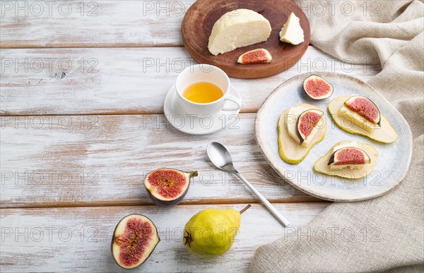 Summer appetizer with pear, cottage cheese, figs and honey on a white wooden background and linen textile. Side view, copy space