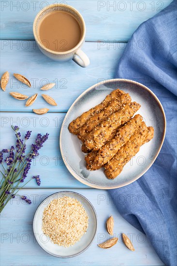 Crumble cookies with seasme and almonds on ceramic plate with cup of coffee and blue linen textile on blue wooden background. top view, flat lay, close up