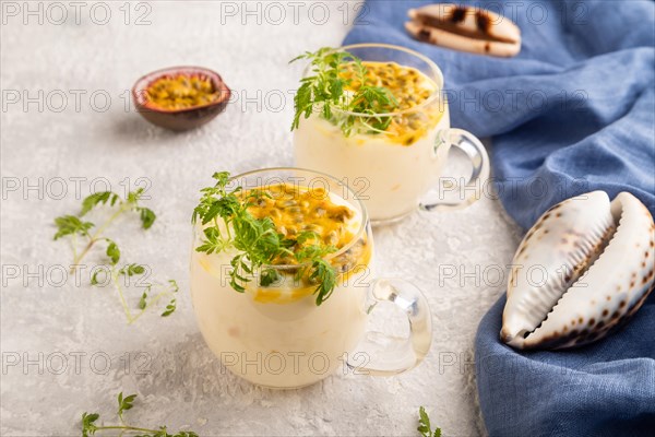 Yogurt with passionfruit and marigold microgreen in glass on gray concrete background with blue linen textile. Side view, close up