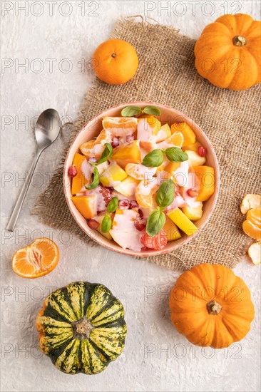 Vegetarian fruit salad of yogurt pumpkin, tangerine, pomegranate, grapefruit, basil microgreen sprouts on gray concrete background and linen textile. Top view, flat lay, close up