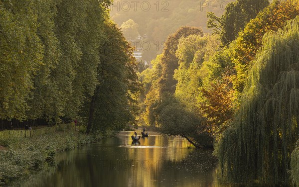 A boat sails on a calm river surrounded by trees in autumn colours