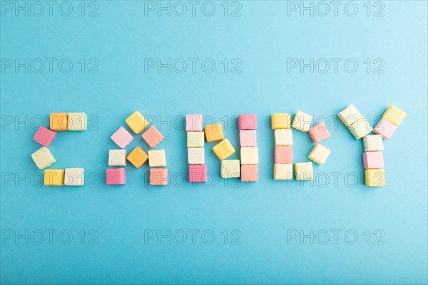 The inscription candy laid out with various fruit jelly chewing candies on blue pastel background. apple, banana, tangerine, top view, flat lay, copy space