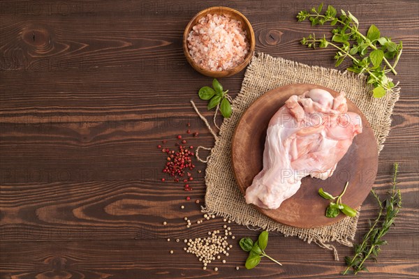 Raw turkey wing with herbs and spices on a wooden cutting board on a brown wooden background and linen textile. Top view, flat lay, copy space