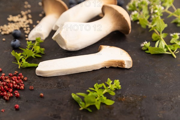 King Oyster mushrooms or Eringi (Pleurotus eryngii) on black concrete background with blueberry, herbs and spices. Side view, selective focus