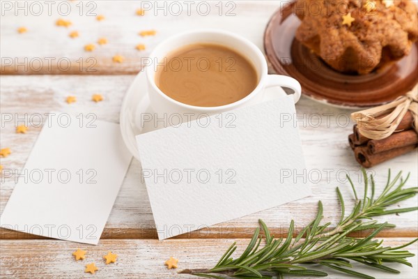 White paper business card mockup with cup of coffee and cake on white wooden background. Blank, side view, still life