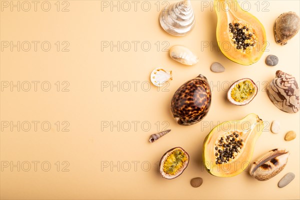 Ripe cut papaya, passion fruit, seashells, pebbles on orange pastel background. Top view, flat lay, copy space. Tropical, healthy food, vacation, holidays concept